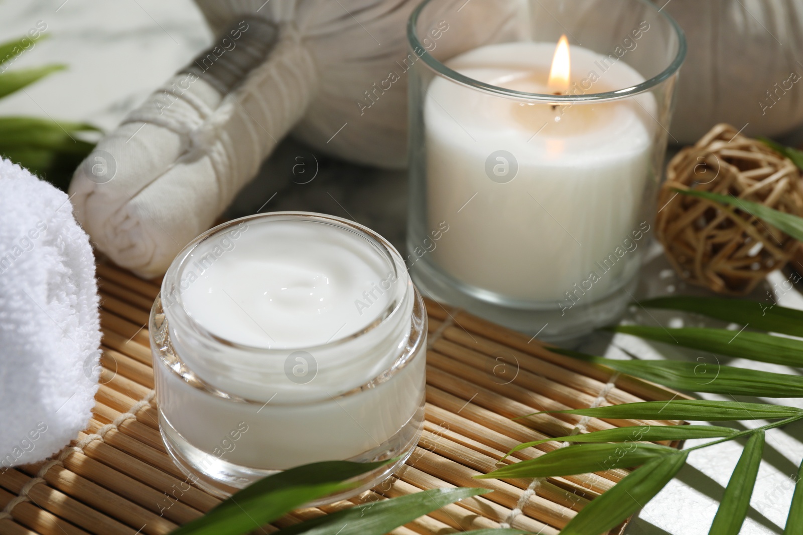 Photo of Spa composition with different cosmetic products, herbal bags, burning candle and leaves on table, closeup