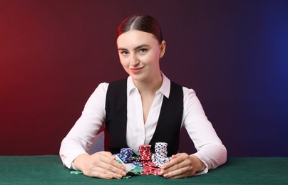 Photo of Professional croupier with casino chips and playing cards at gambling table on color background