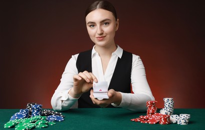 Photo of Professional croupier with chips shuffling playing cards at gambling table on color background