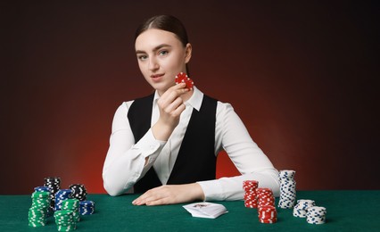 Professional croupier with casino chips and playing cards at gambling table on color background