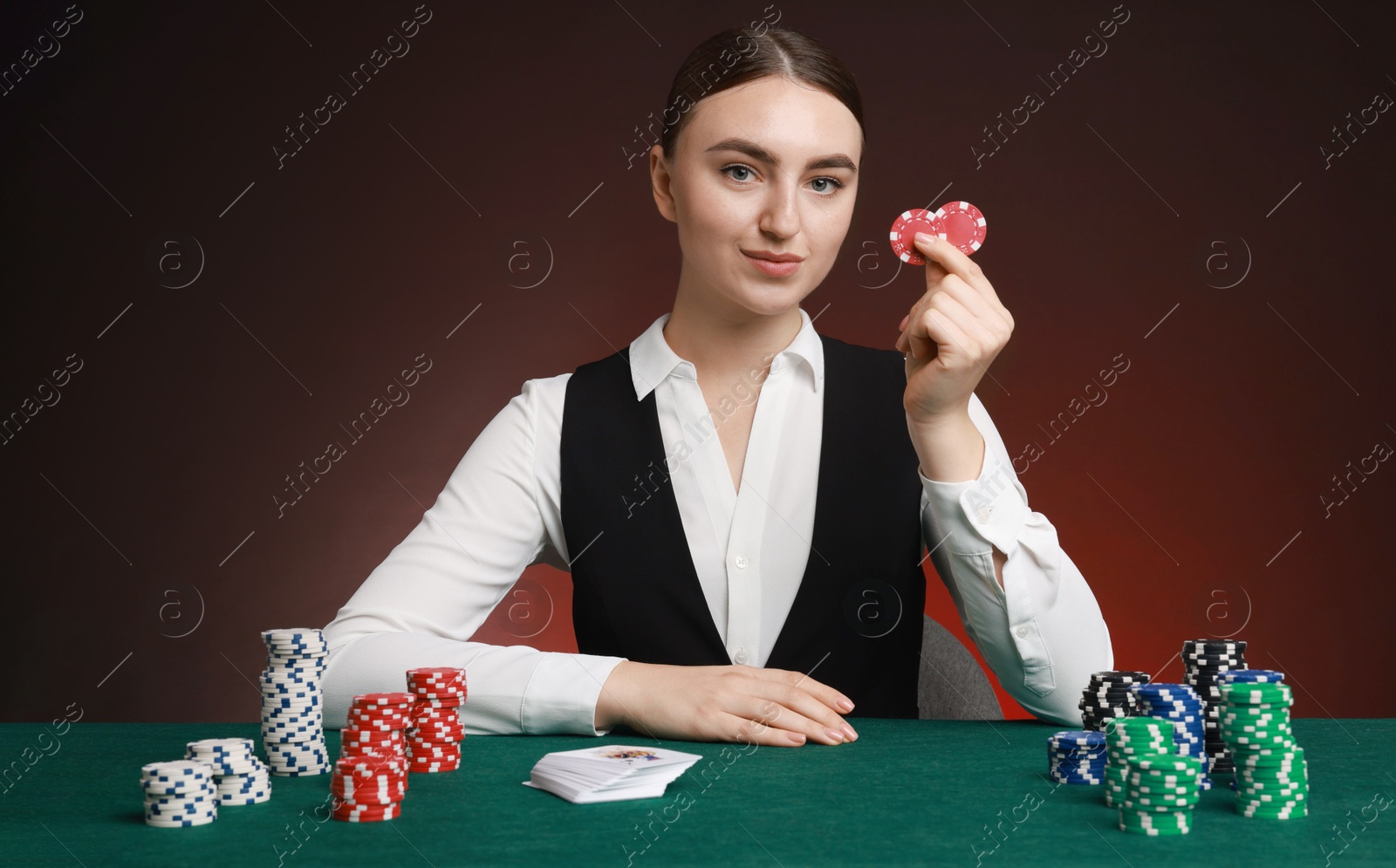 Photo of Professional croupier with casino chips and playing cards at gambling table on color background