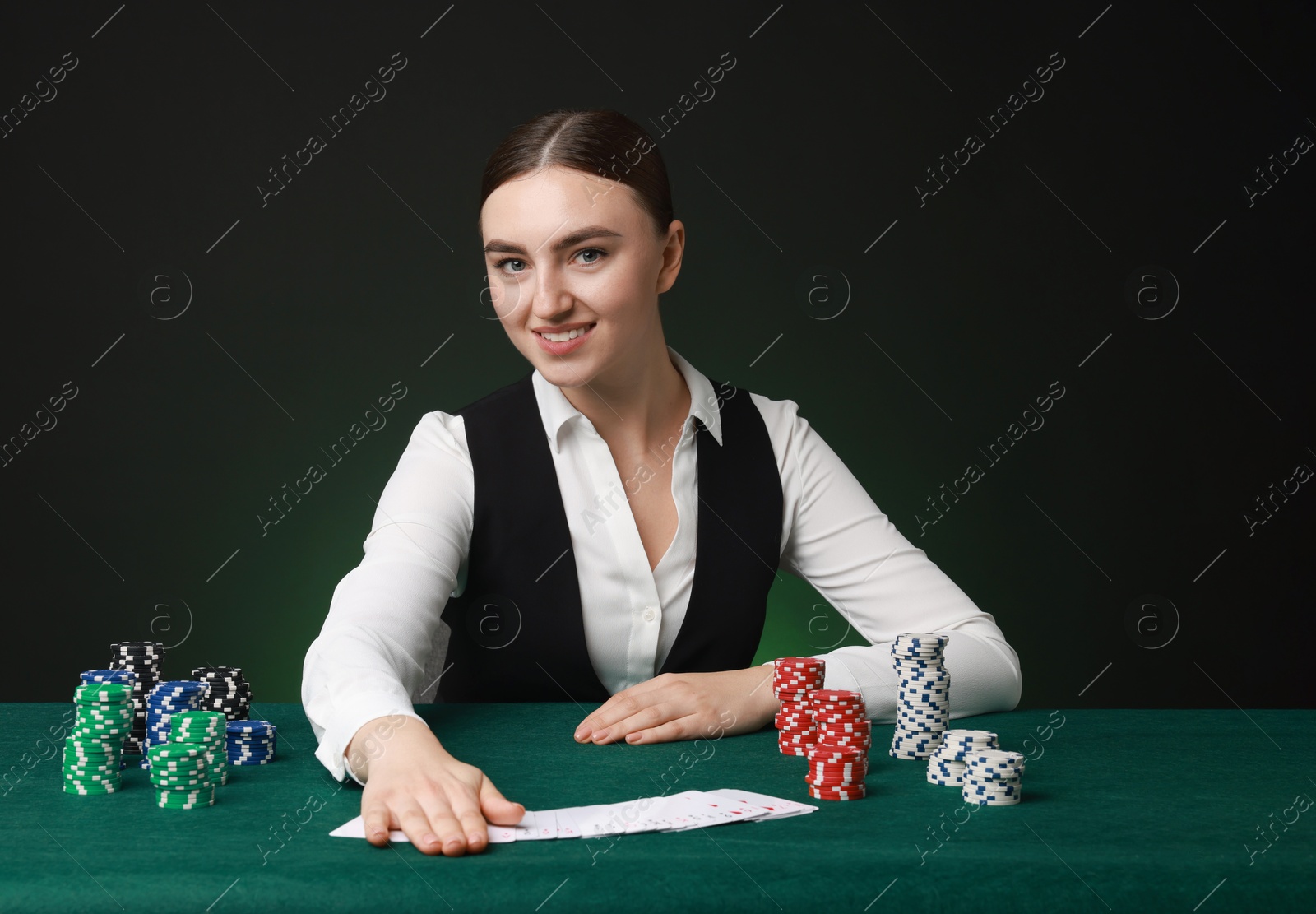 Photo of Professional croupier with casino chips and playing cards at gambling table on color background