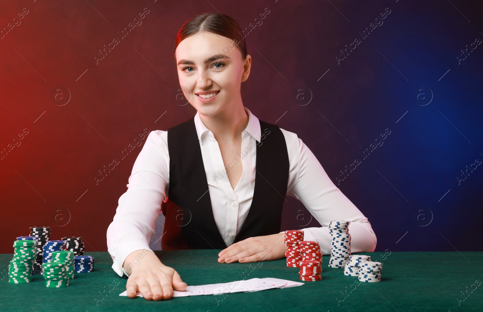 Photo of Professional croupier with casino chips and playing cards at gambling table on color background with smoke