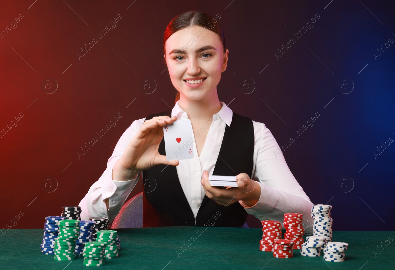 Photo of Professional croupier with casino chips and playing cards at gambling table on color background