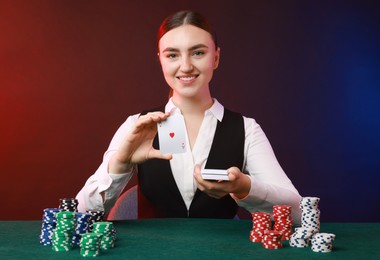 Professional croupier with casino chips and playing cards at gambling table on color background