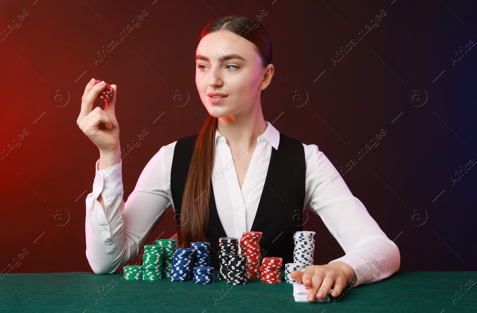 Photo of Professional croupier with casino chips and playing cards at gambling table on color background