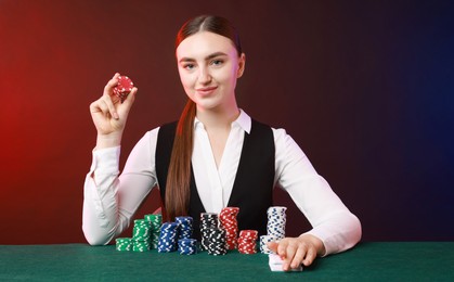 Photo of Professional croupier with casino chips and playing cards at gambling table on color background