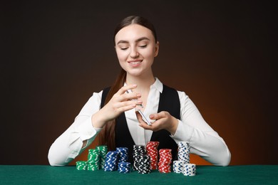 Professional croupier with casino chips and playing cards at gambling table on color background