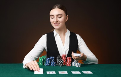 Professional croupier with casino chips and playing cards at gambling table on color background