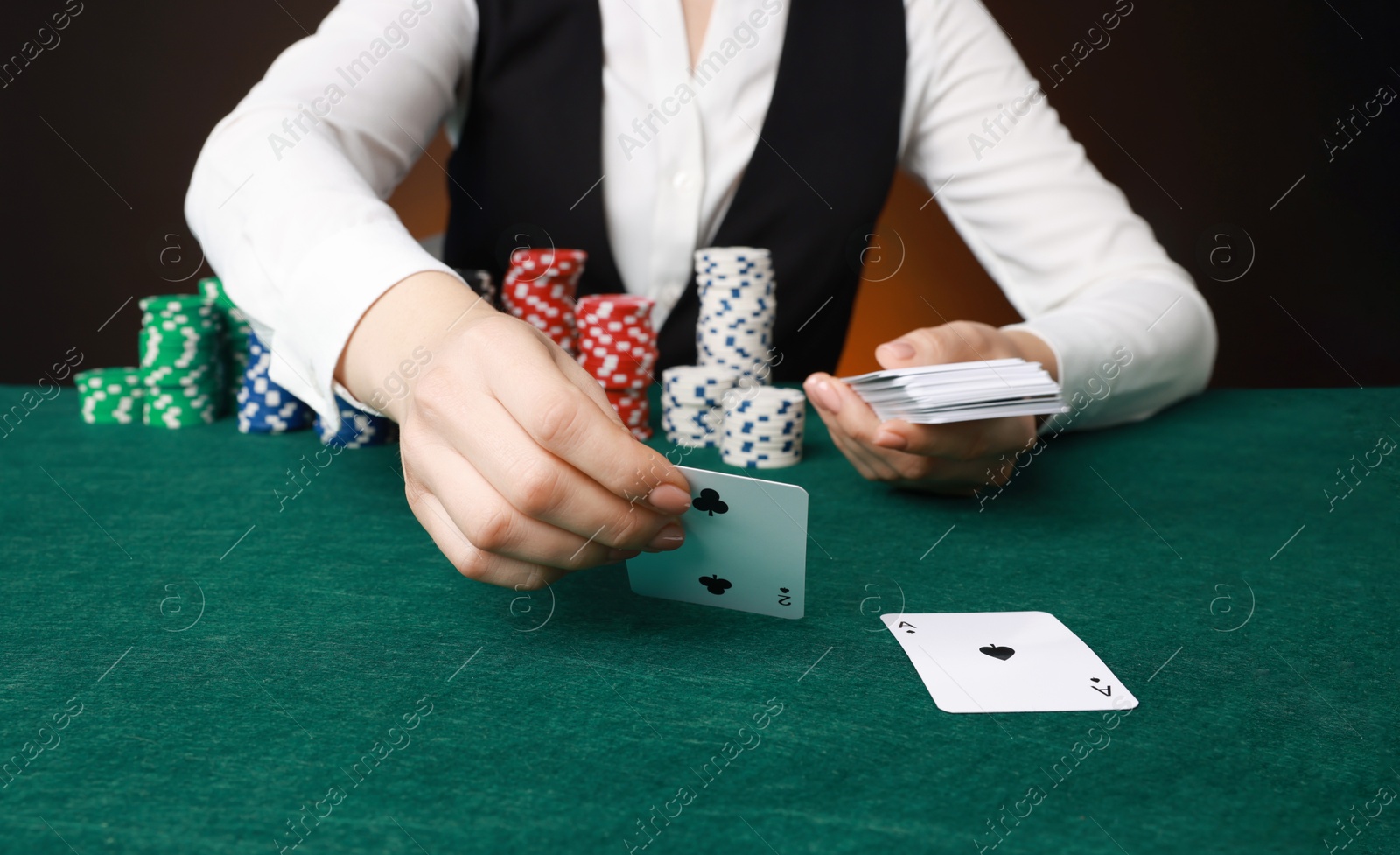 Photo of Professional croupier with casino chips and playing cards at gambling table on color background, closeup