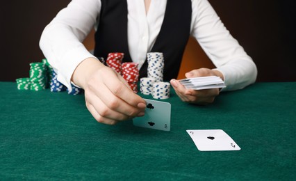 Professional croupier with casino chips and playing cards at gambling table on color background, closeup