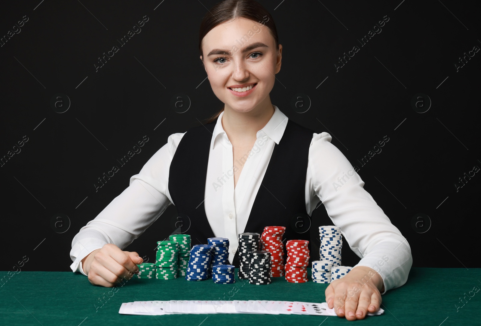 Photo of Professional croupier with casino chips and playing cards at gambling table on black background