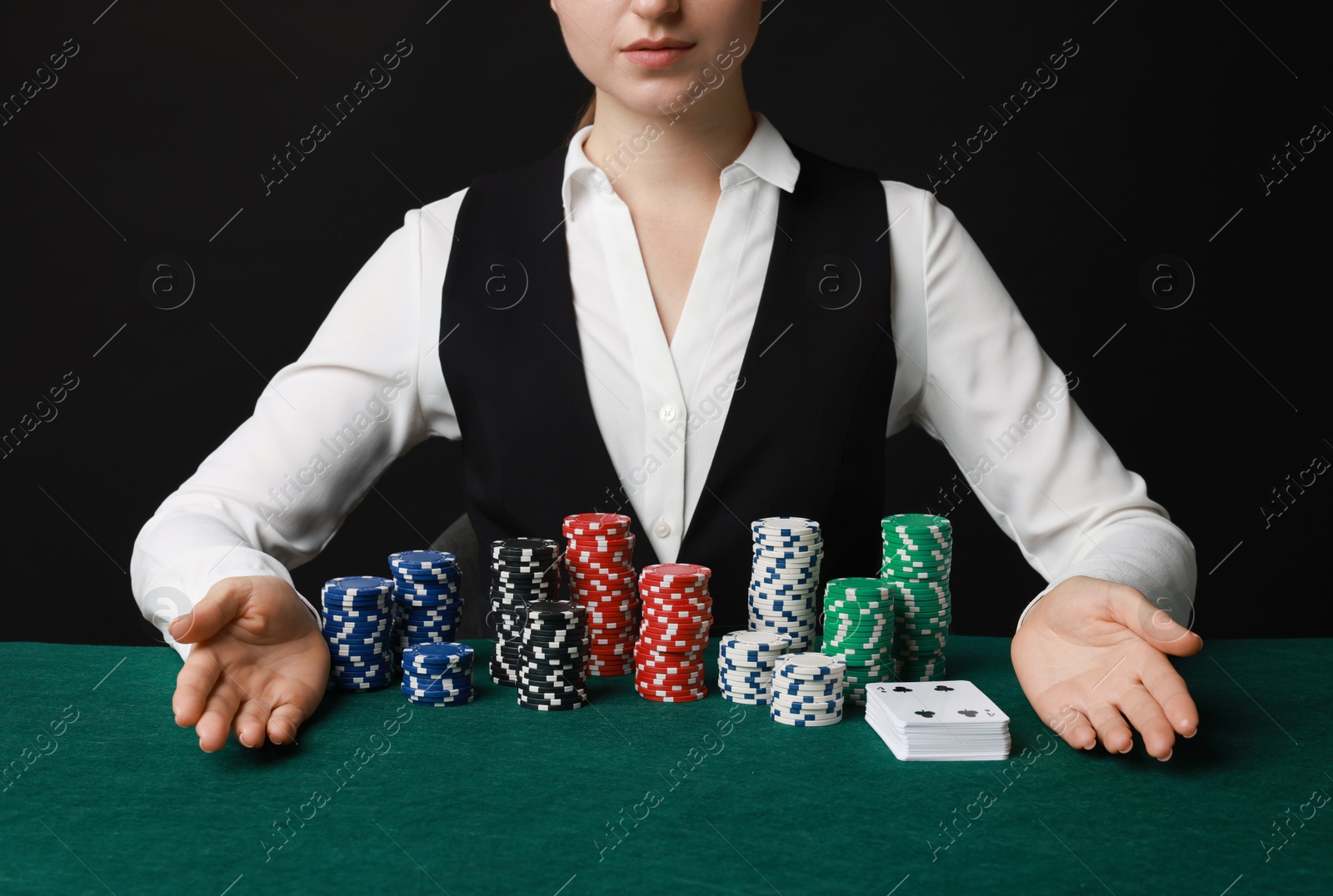 Photo of Professional croupier with casino chips and playing cards at gambling table on black background, closeup