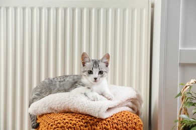 Photo of Cute little kitten on pouf near radiator at home