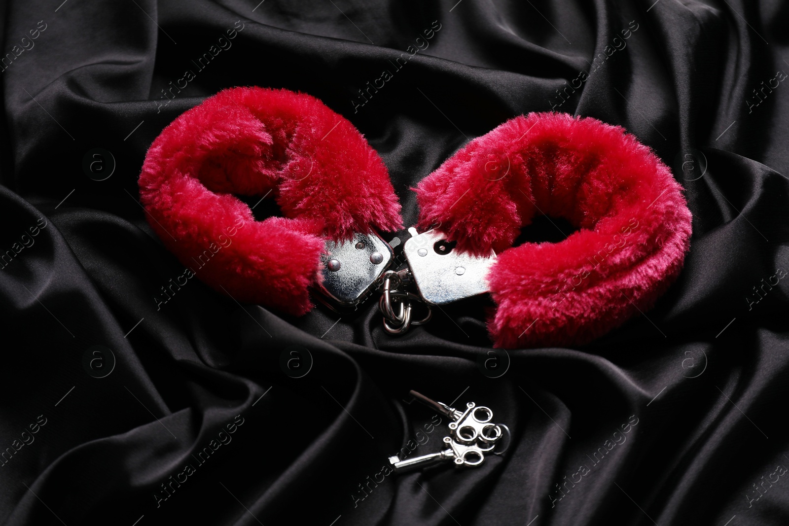 Photo of Red fluffy handcuffs and keys on black fabric