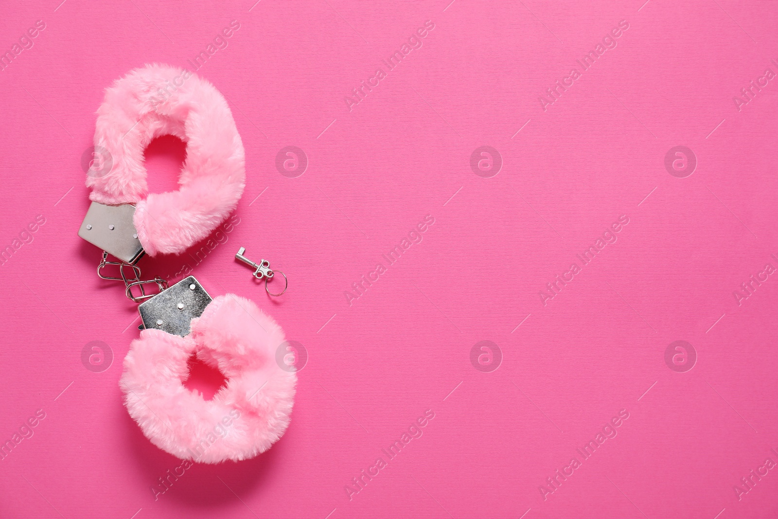 Photo of Fluffy handcuffs and key on pink background, top view. Space for text