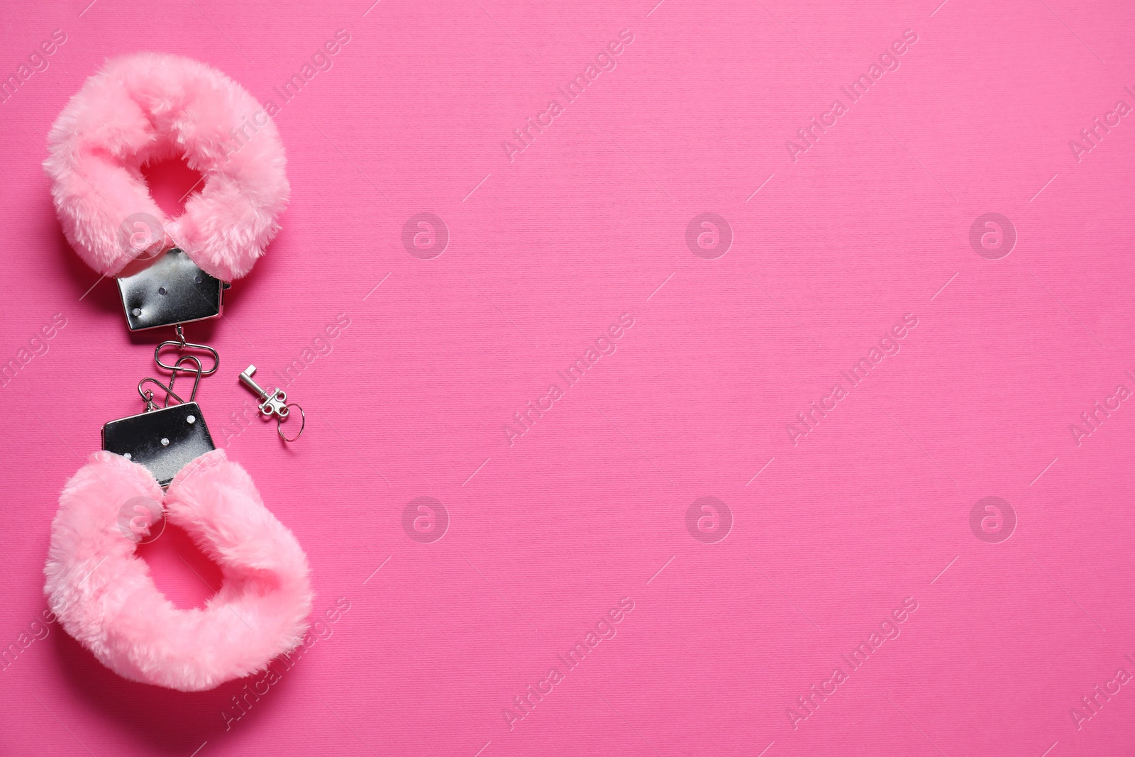 Photo of Fluffy handcuffs and key on pink background, top view. Space for text