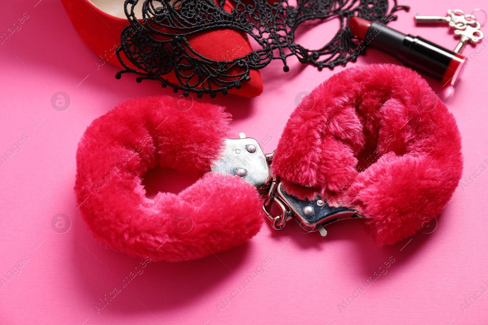 Photo of Red fluffy handcuffs, shoes, lace mask, lipstick and keys on pink background, closeup