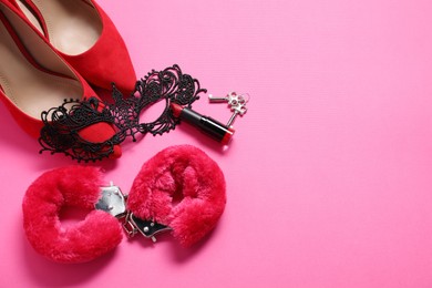 Photo of Red fluffy handcuffs, keys, lace mask, shoes and lipstick on pink background, flat lay. Space for text