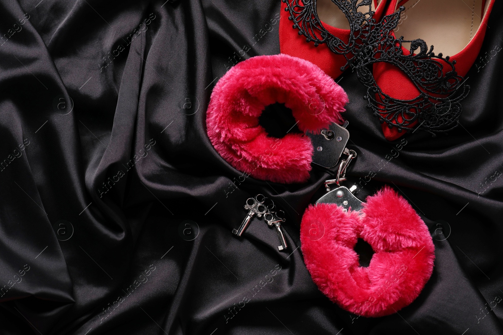 Photo of Red fluffy handcuffs, keys, shoes and lace mask on black fabric, flat lay. Space for text