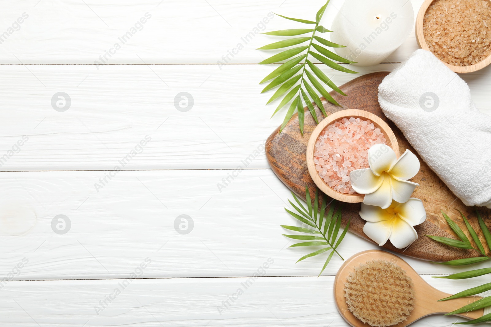 Photo of Spa composition with sea salt, plumeria flowers and burning candle on white wooden table, flat lay. Space for text