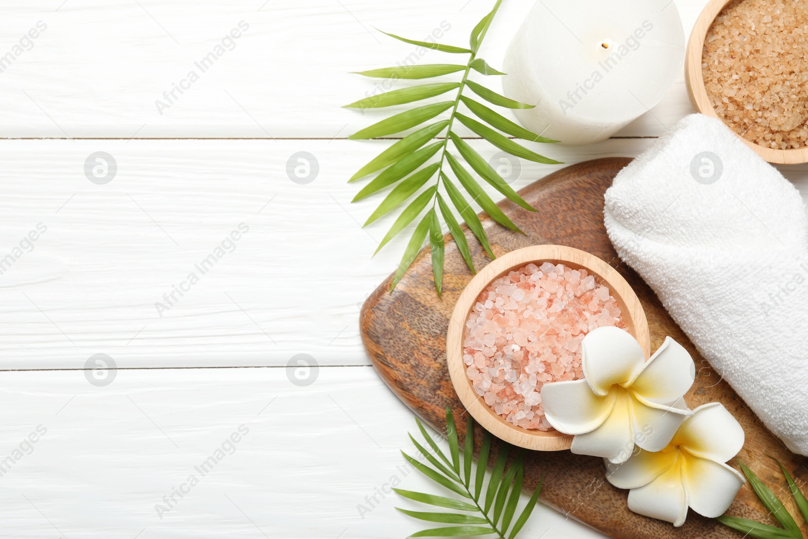 Photo of Spa composition with sea salt, plumeria flowers and burning candle on white wooden table, flat lay. Space for text