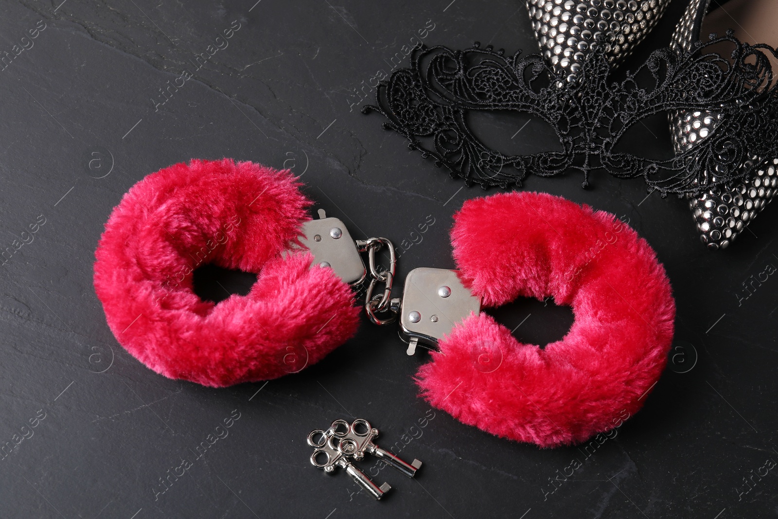 Photo of Red fluffy handcuffs, keys, shoes and lace mask on black surface, above view