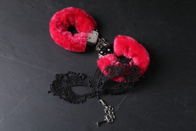 Photo of Red fluffy handcuffs, keys and lace mask on black surface, above view