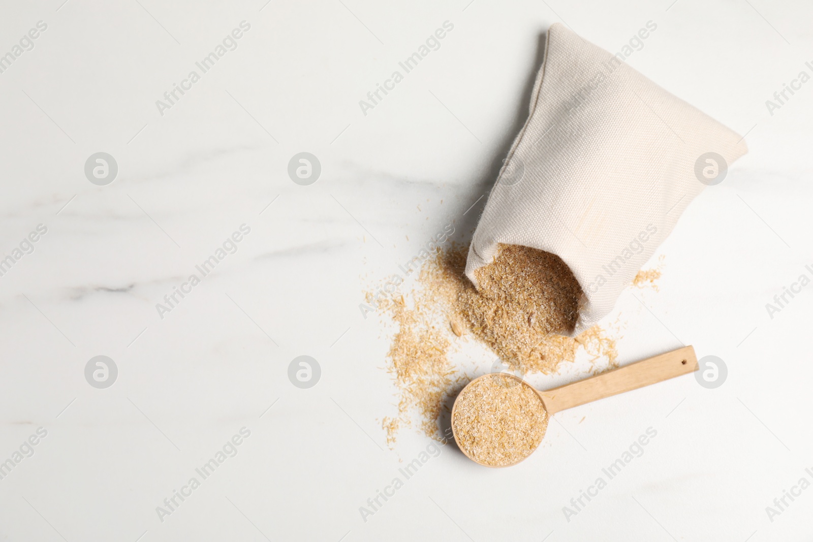 Photo of Oat bran in burlap bag and wooden spoon on white marble table, top view. Space for text