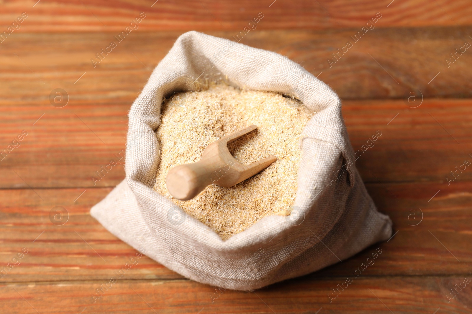 Photo of Oat bran and scoop in burlap bag on wooden table, closeup