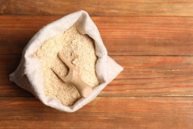 Photo of Oat bran and scoop in burlap bag on wooden table, top view. Space for text