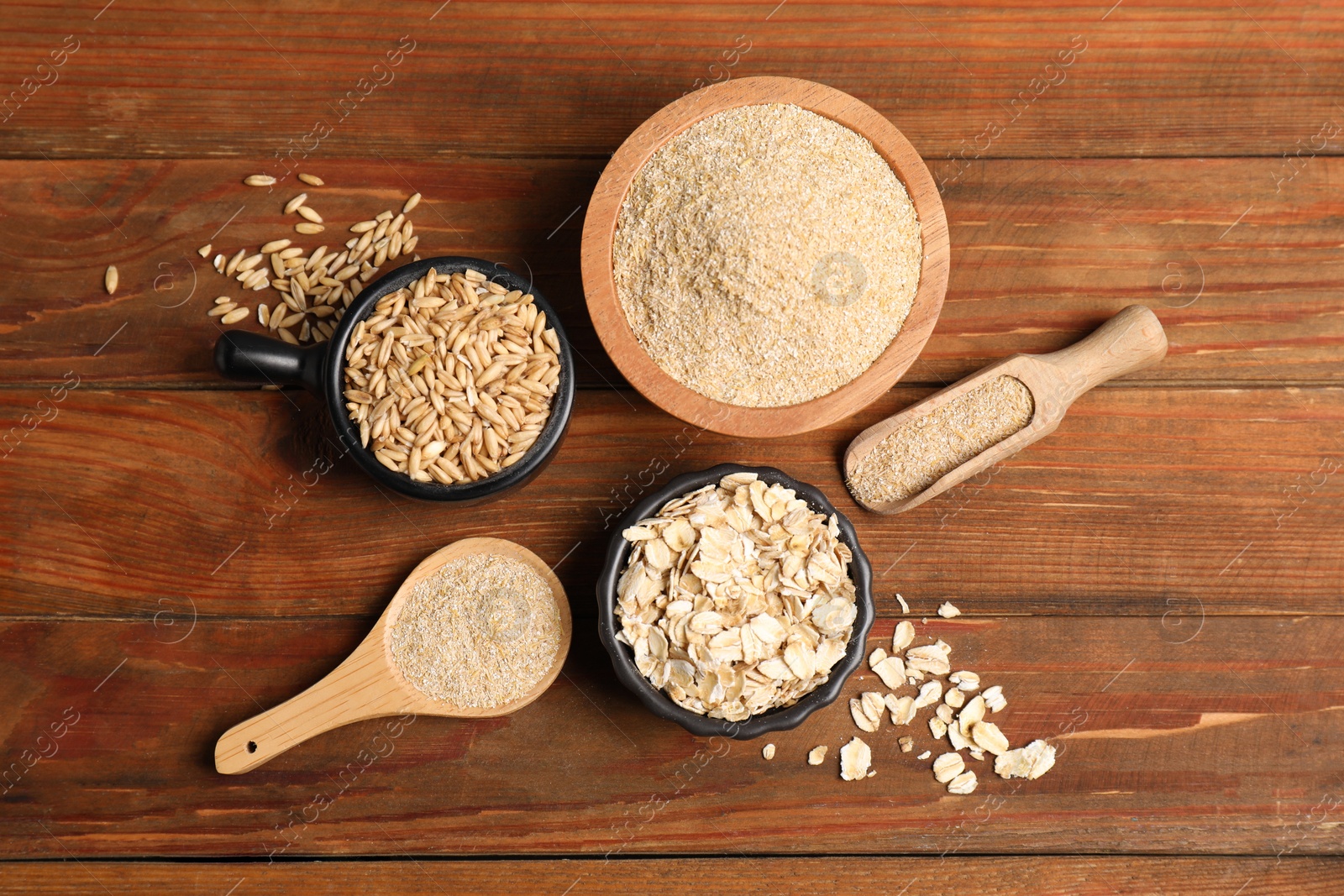 Photo of Oat bran, flakes and grains on wooden table, flat lay