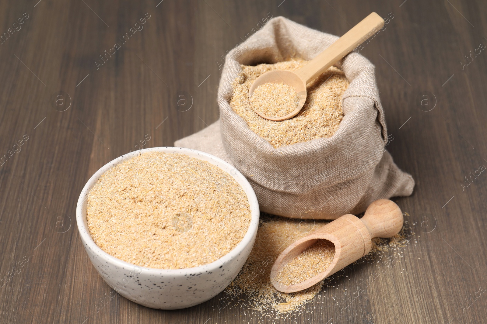 Photo of Oat bran in bowl, scoop, spoon and burlap bag on wooden table