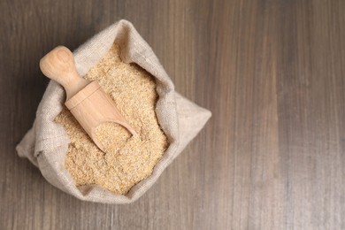 Photo of Oat bran and scoop in burlap bag on wooden table, top view. Space for text