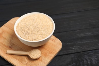 Photo of Oat bran in bowl and spoon on black wooden table, space for text