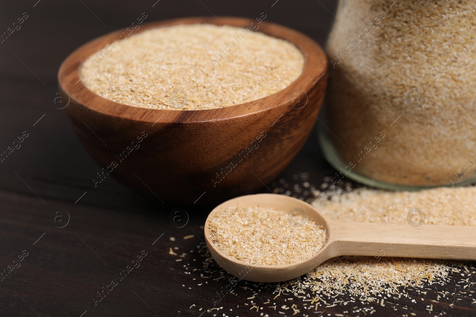 Photo of Oat bran in bowl, spoon and glass jar on wooden table, closeup