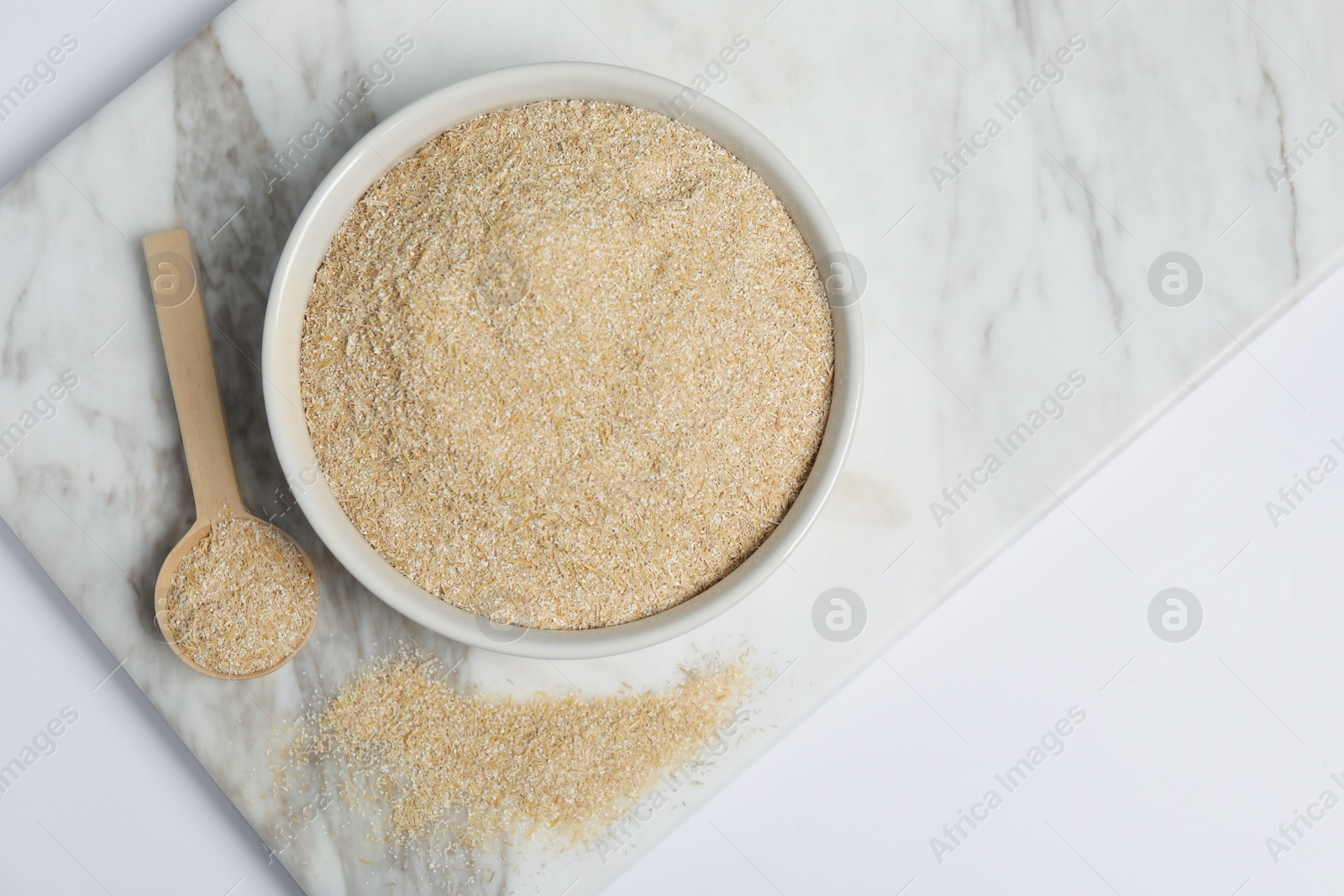 Photo of Oat bran in bowl and spoon on white table, top view