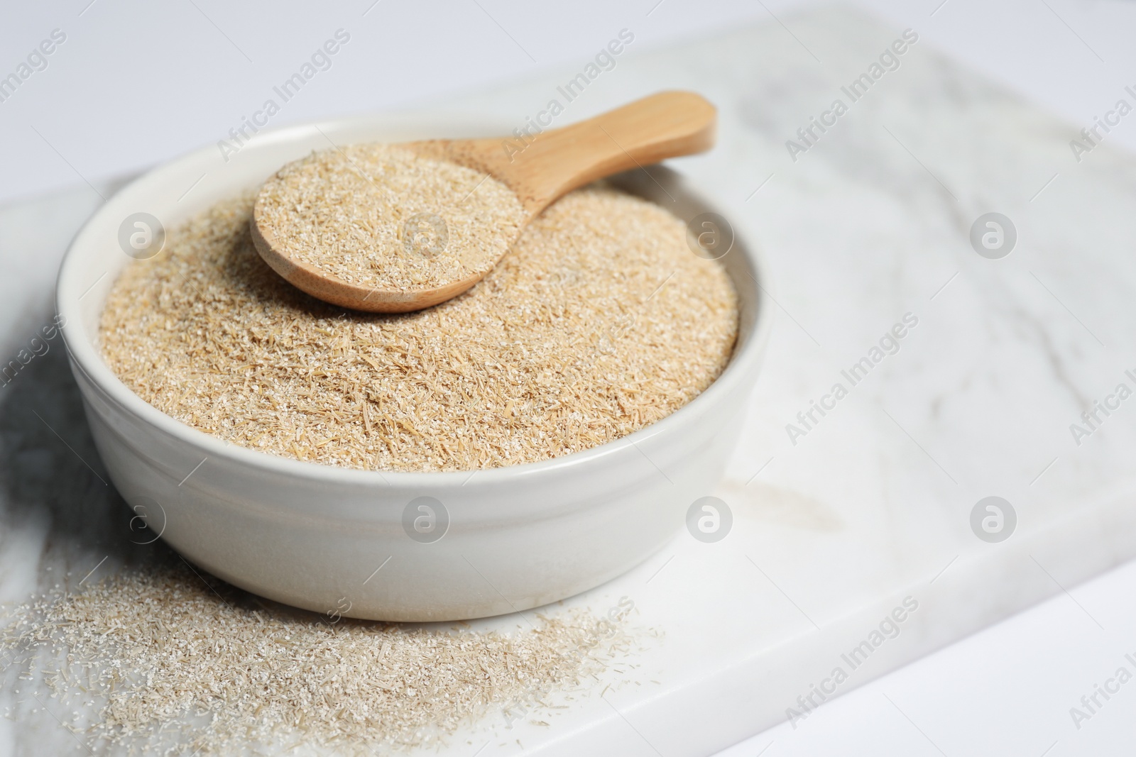 Photo of Oat bran in bowl and spoon on white table, closeup