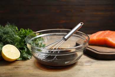 Photo of Soy sauce in bowl, whisk, salmon fillet, herbs and lemon on wooden table