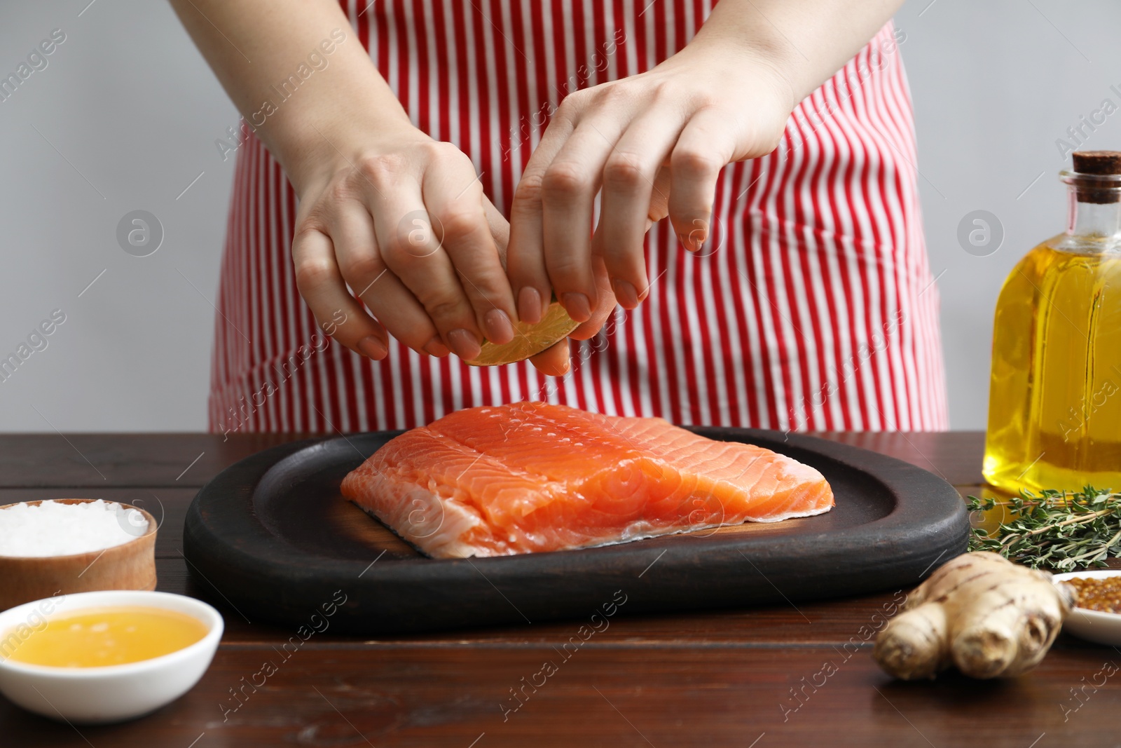 Photo of Woman squeezing lime juice onto salmon fillet at wooden table, closeup