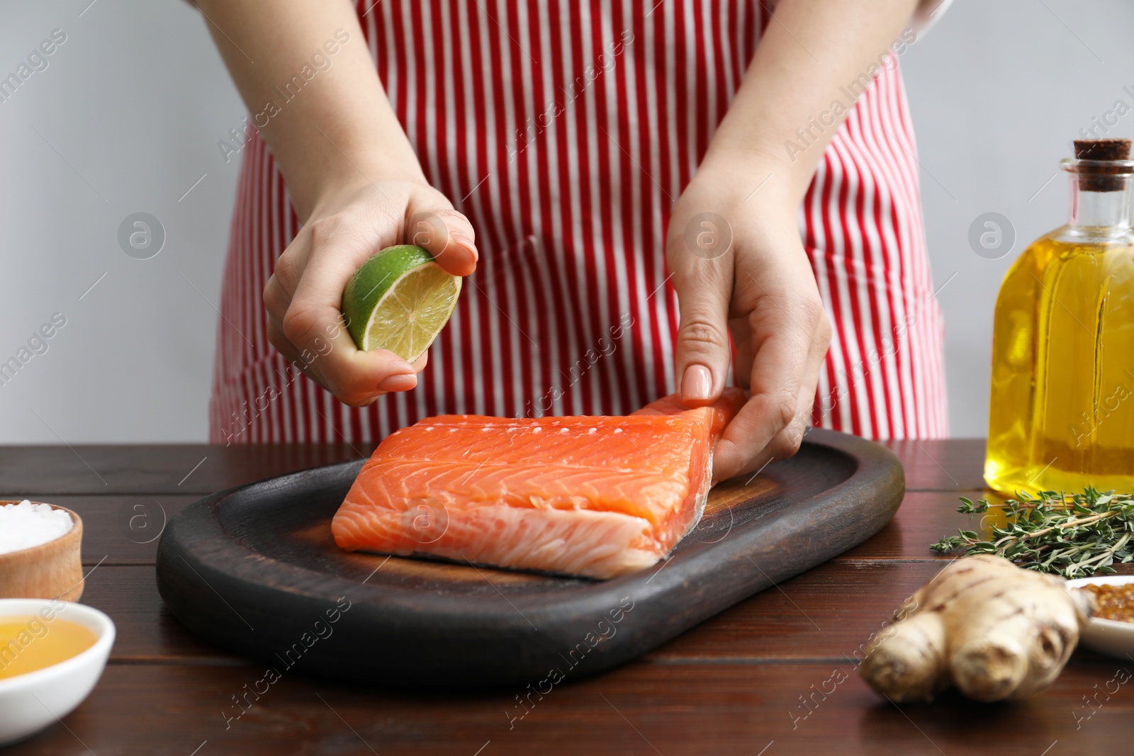 Photo of Woman squeezing lime juice onto salmon fillet at wooden table, closeup