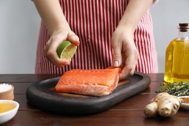 Photo of Woman squeezing lime juice onto salmon fillet at wooden table, closeup