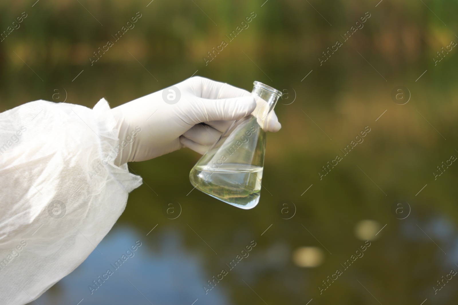 Photo of Examination of water quality. Researcher holding flask with sample outdoors, closeup