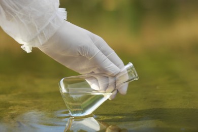 Photo of Examination of water quality. Researcher taking water sample from lake outdoors, closeup