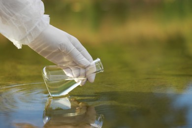 Photo of Examination of water quality. Researcher taking water sample from lake outdoors, closeup. Space for text