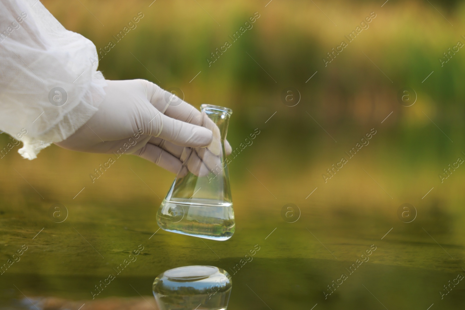 Photo of Examination of water quality. Researcher holding flask with sample from lake outdoors, closeup. Space for text