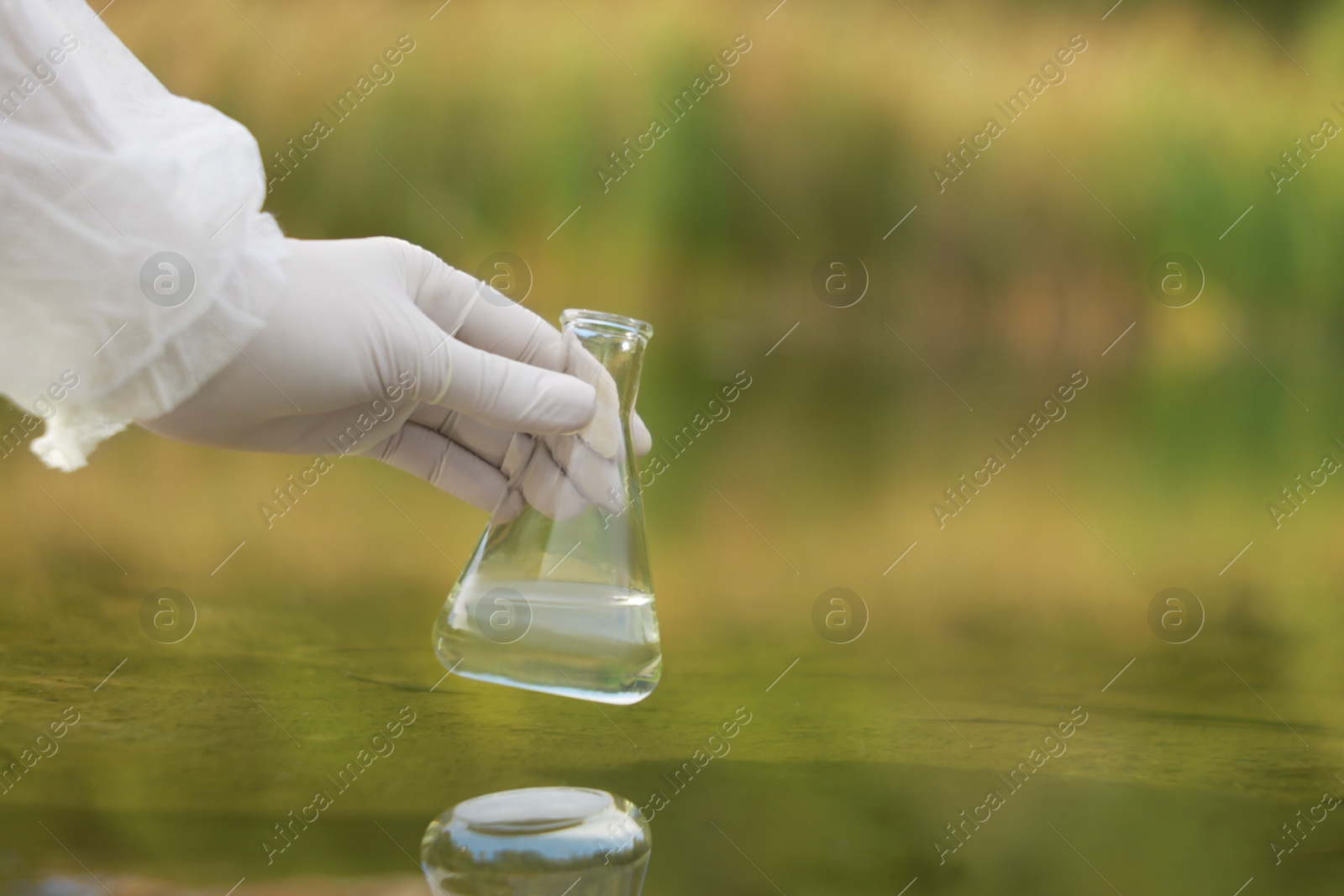 Photo of Examination of water quality. Researcher holding flask with sample from lake outdoors, closeup. Space for text