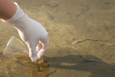 Photo of Examination of water quality. Researcher taking water sample from lake outdoors, closeup. Space for text