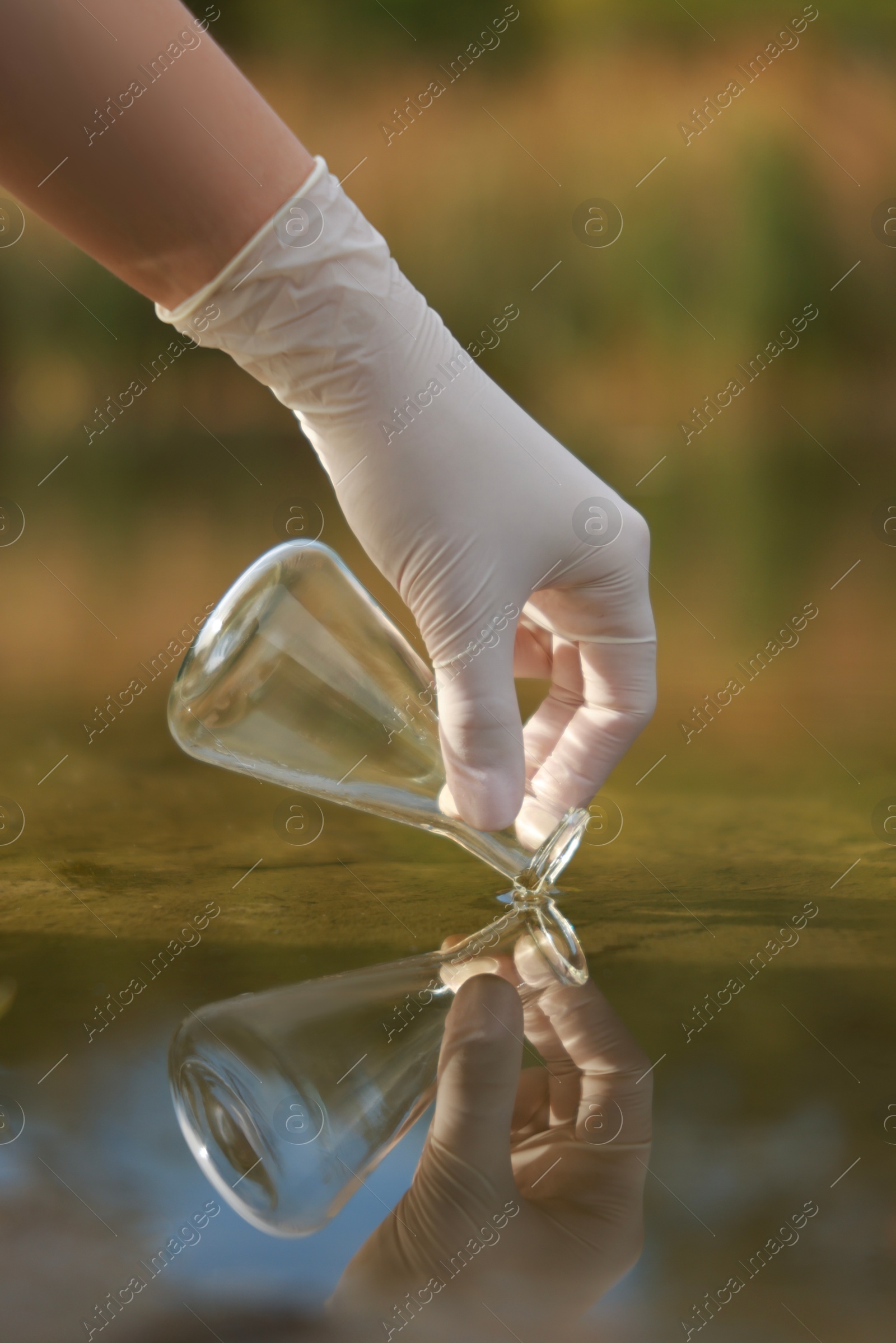 Photo of Examination of water quality. Researcher taking water sample from lake outdoors, closeup