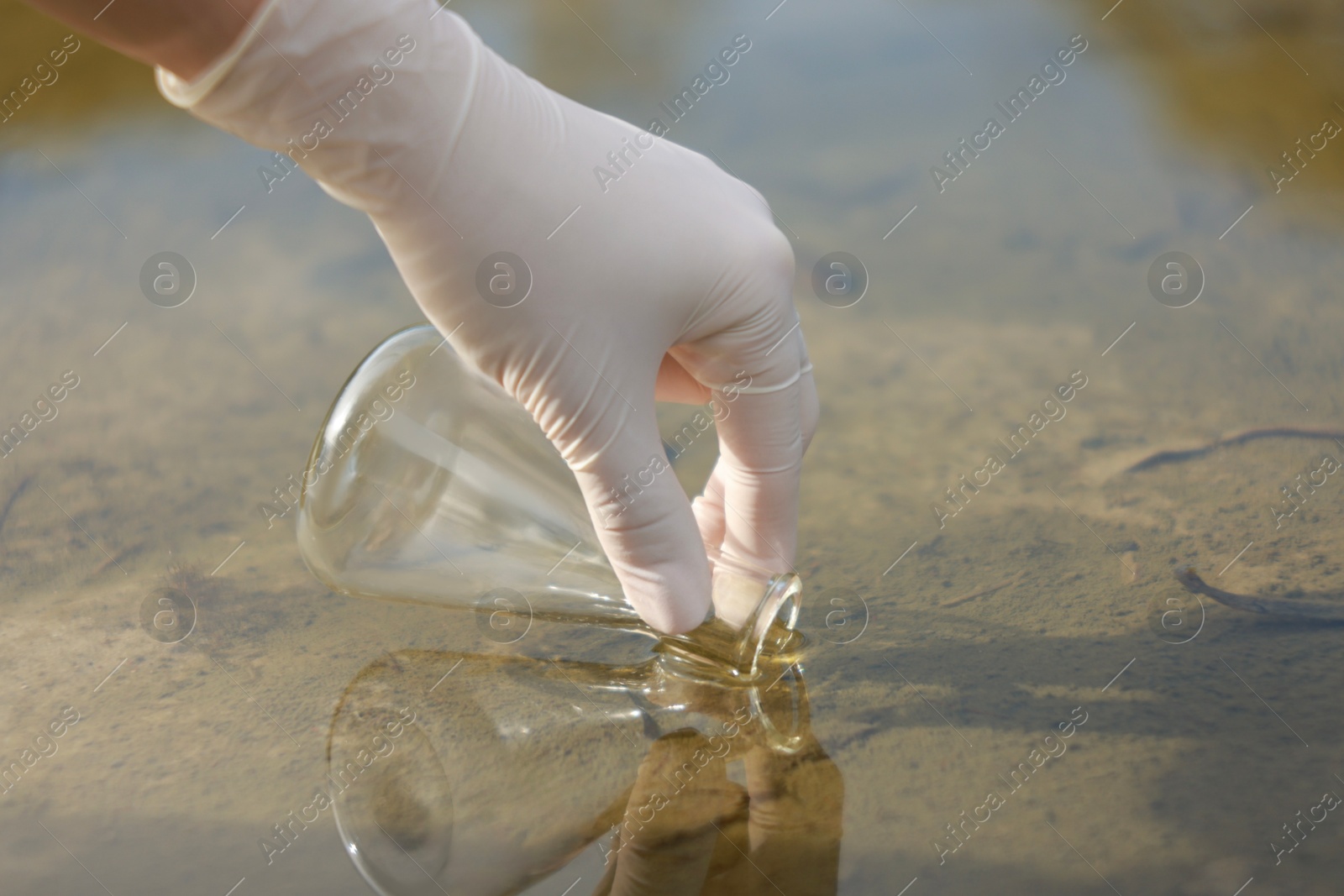 Photo of Examination of water quality. Researcher taking water sample from lake outdoors, closeup